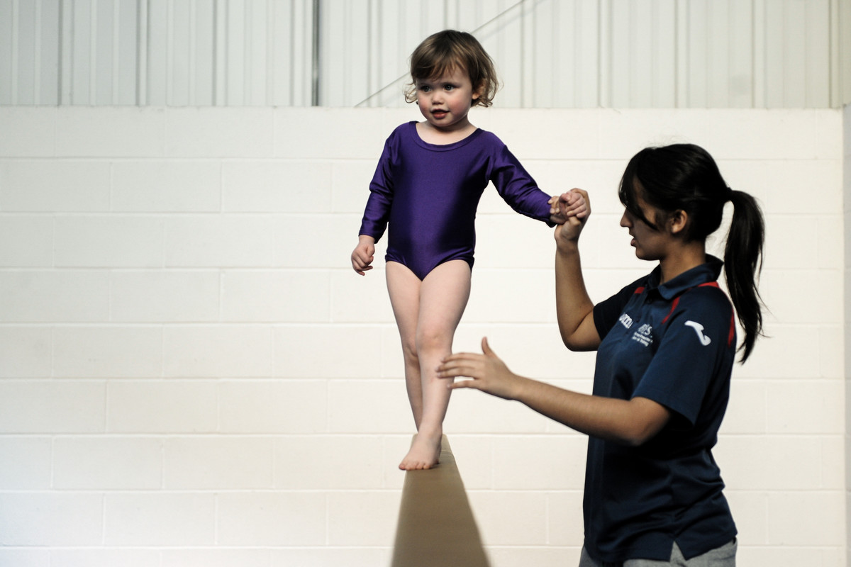 pre-school gymnast gets an early experience on the beam, developing balance and 